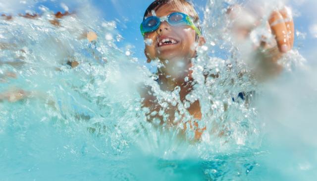 Junge mit Schwimmbrille planscht im Wasser